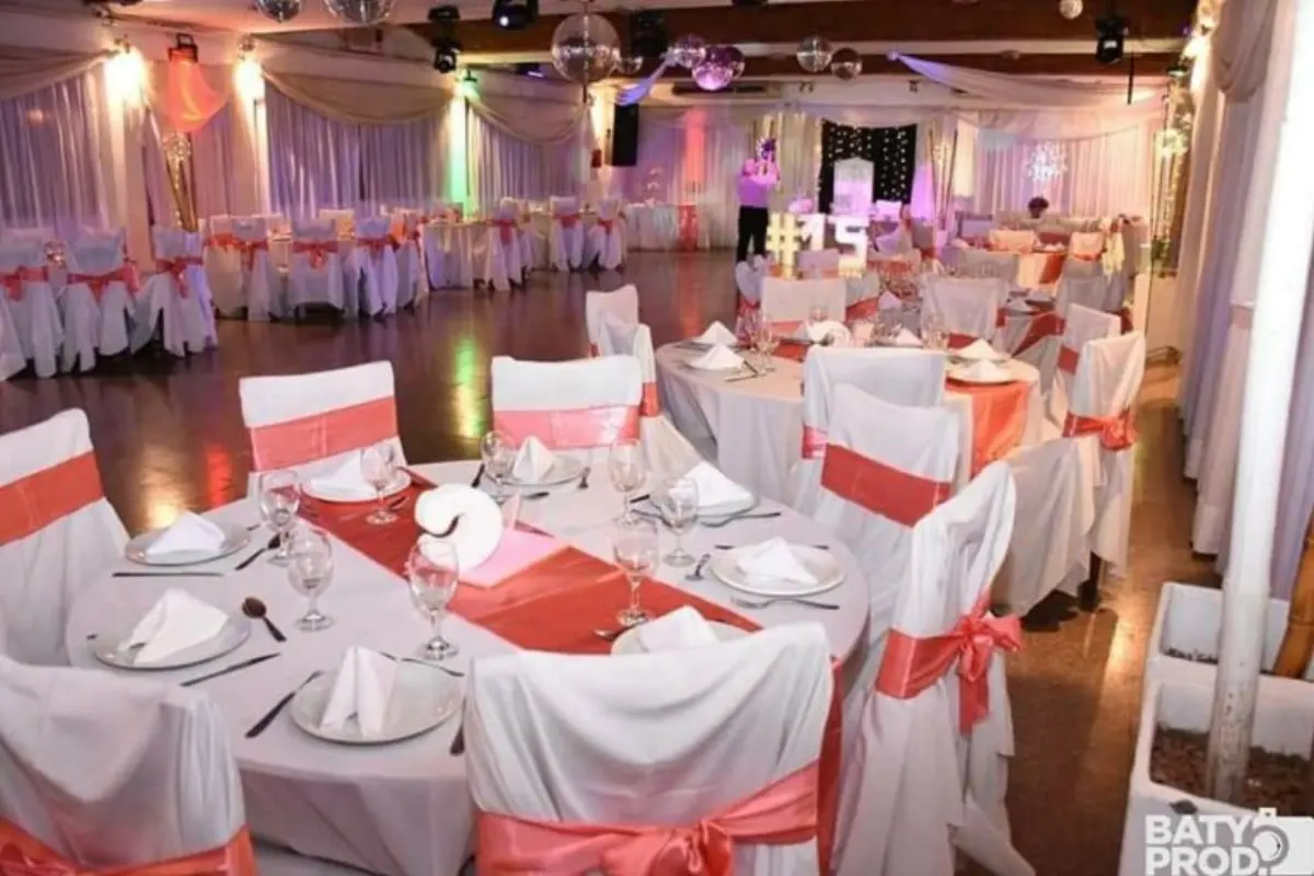 Mesas redondas montadas con mantelería blanca y moños coral en el salón